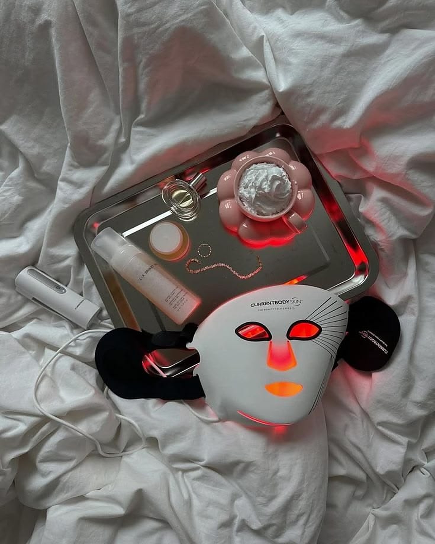 LED light therapy face mask laid out with skincare on white linen