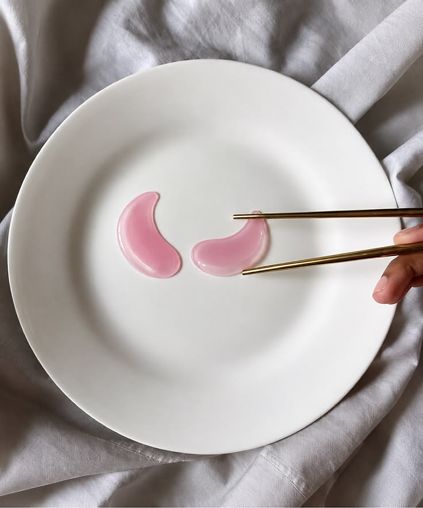 Pink under-eye patches on a white plate with gold chopsticks